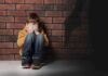 New Footage Reopens Questions In School Shooting boy sitting against brick wall covering his face