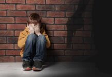 boy sitting against brick wall covering his face