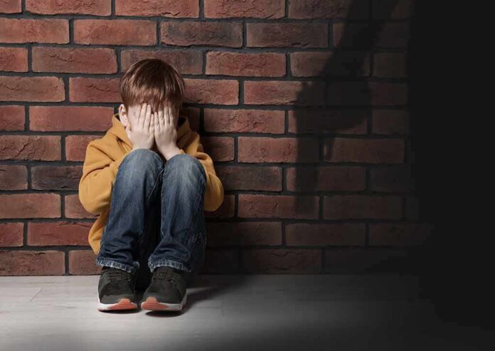 shutterstock_2259362731 boy sitting against brick wall covering his face