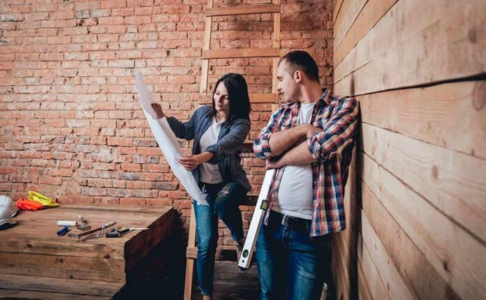 Two people reviewing blueprints in a rustic room under renovation